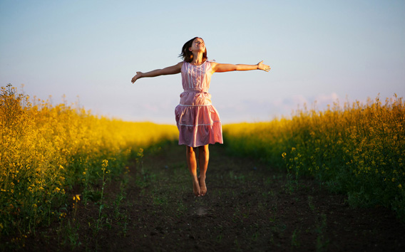 Happy woman jumps to the sky in the yellow meadow at the sunset